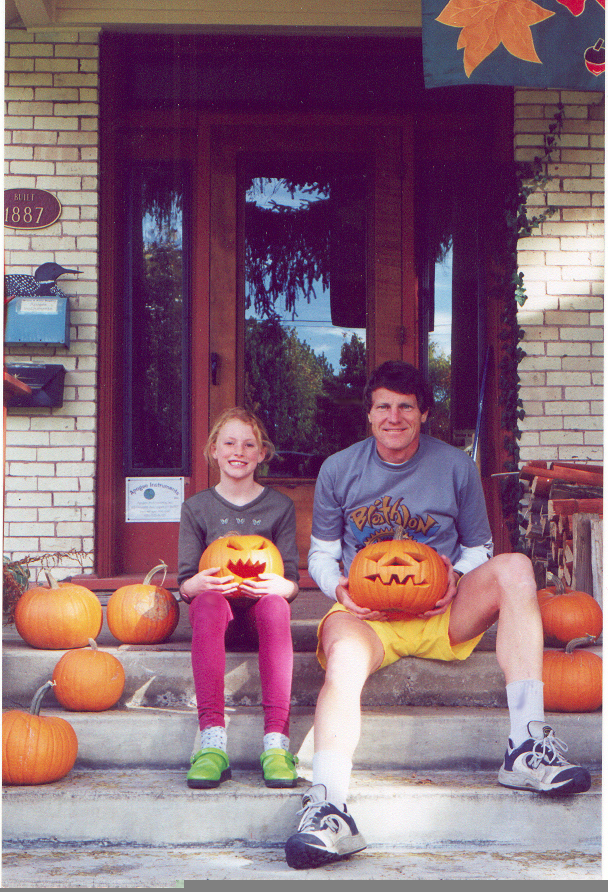 Anna and Bruce Bugbee seated on the porch steps holding jack-o'-lanterns